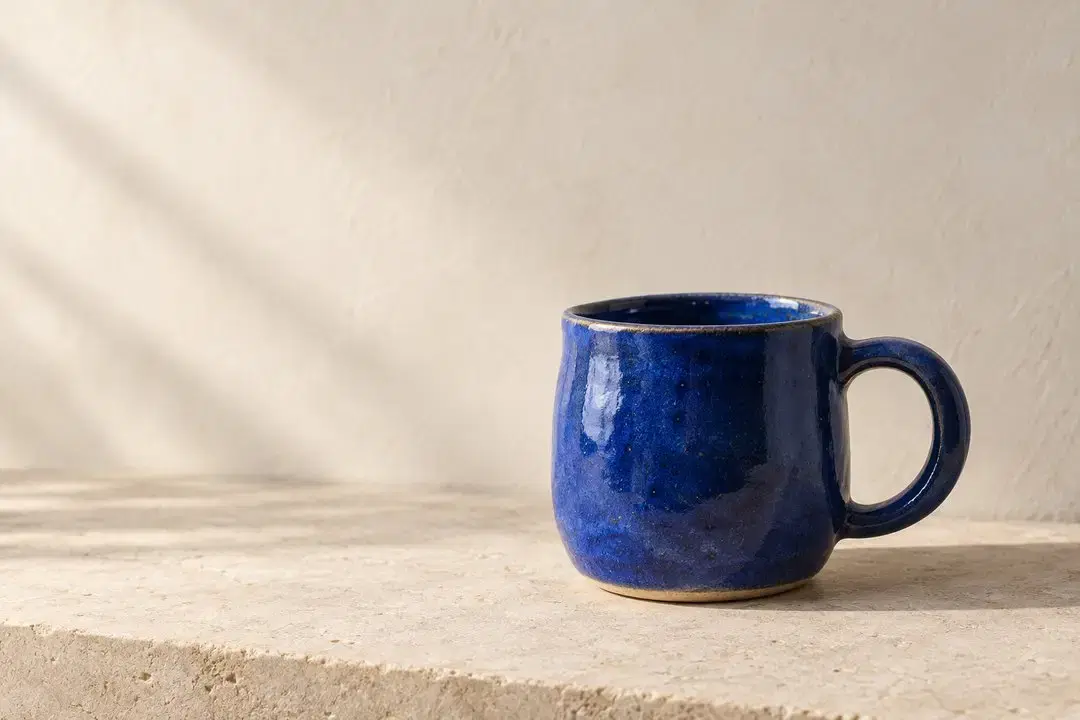 A cobalt-blue ceramic mug on a pale stone ledge, with soft light and open space on the left.